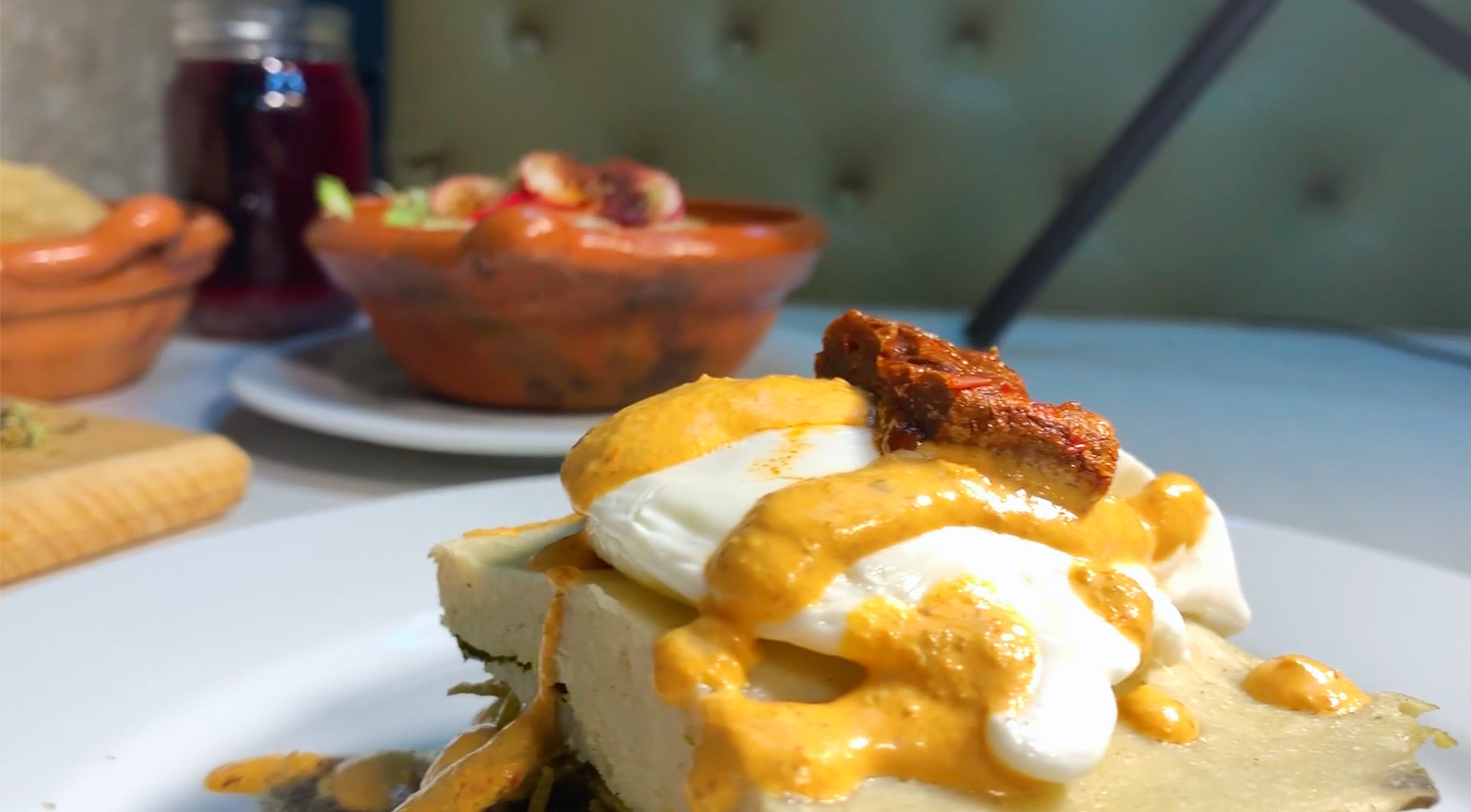 Huevo caudillo con pozole y tostadas al fondo, acompañados de agua de jamaica.